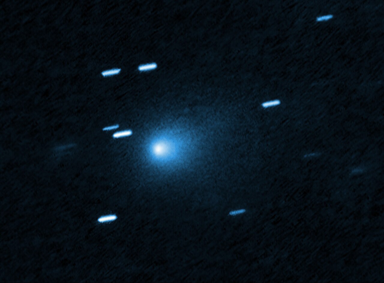 A bright blue-white point with a soft, teardrop-shaped blue haze around it sits just left of center in a dark blue field, with about ten short, pale blue streaks scattered around it.