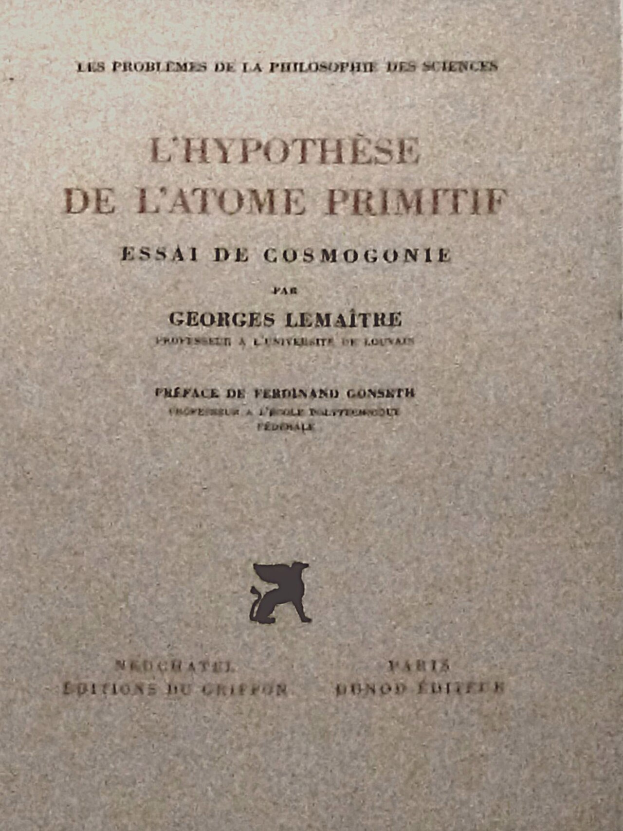 Cover of a speckled gray-beige French book. The title L’Hypothèse de l’Atome primitif is printed in large reddish-brown capital letters, with the subtitle Essai de cosmogonie and the name Georges Lemaître in black below it. A small black griffin emblem sits near the bottom, above the publishers’ names in Neuchâtel and Paris.