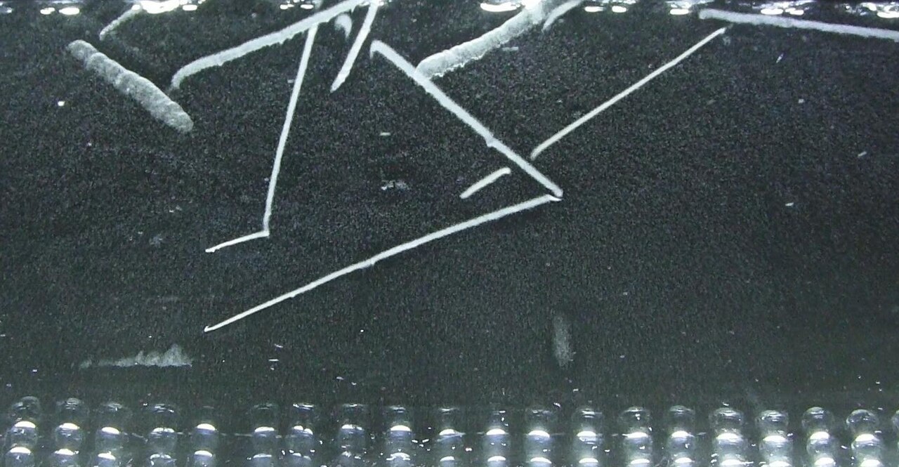 Thin white streaks on a black speckled background, several joined in V shapes, with a row of glowing droplets along the bottom edge.