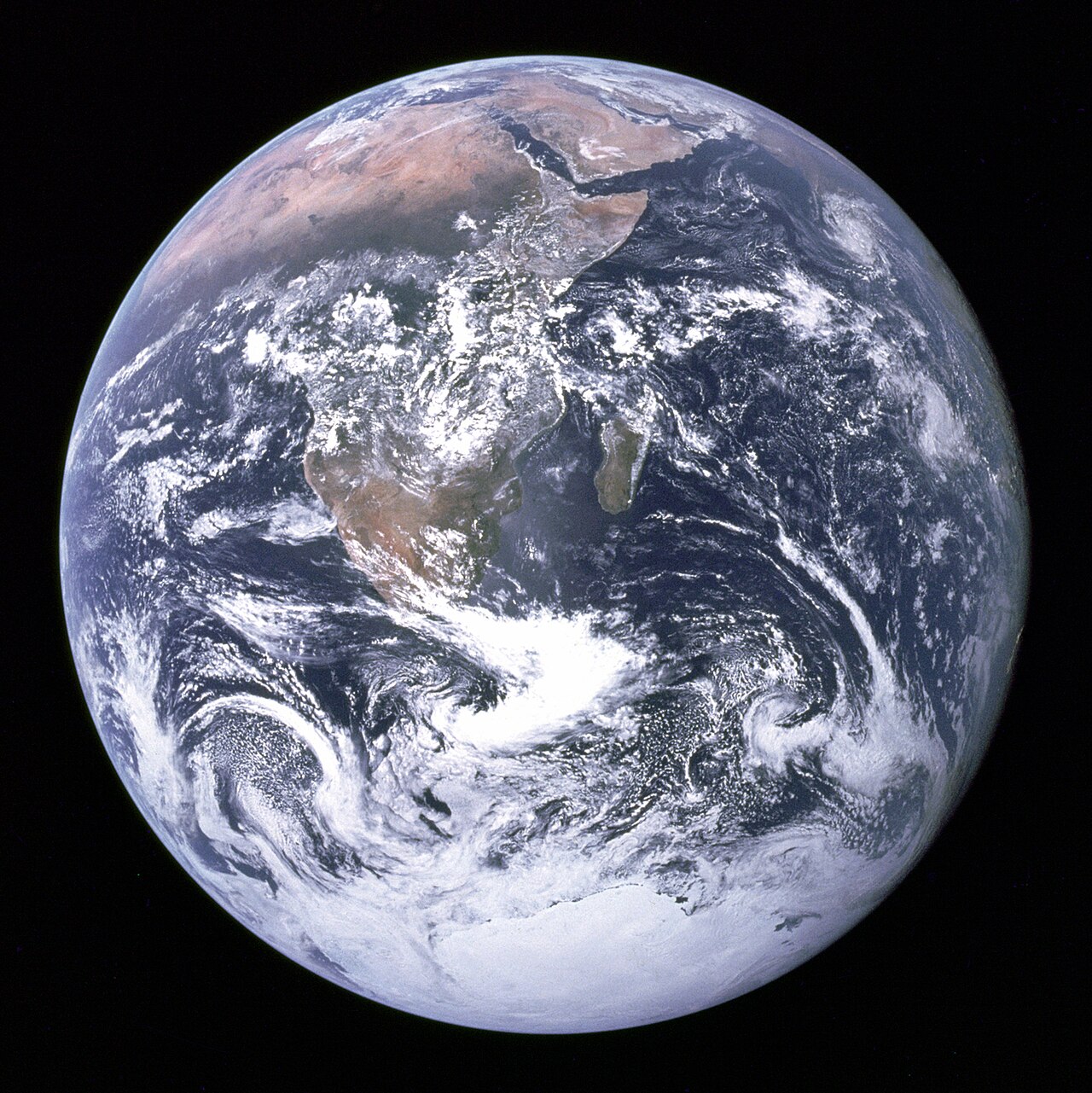 The whole Earth against black space, with the tan and brown land of Africa and the Arabian Peninsula near the top, the island of Madagascar off Africa’s east coast, swirling white clouds over blue ocean, and the white ice of Antarctica at the bottom.