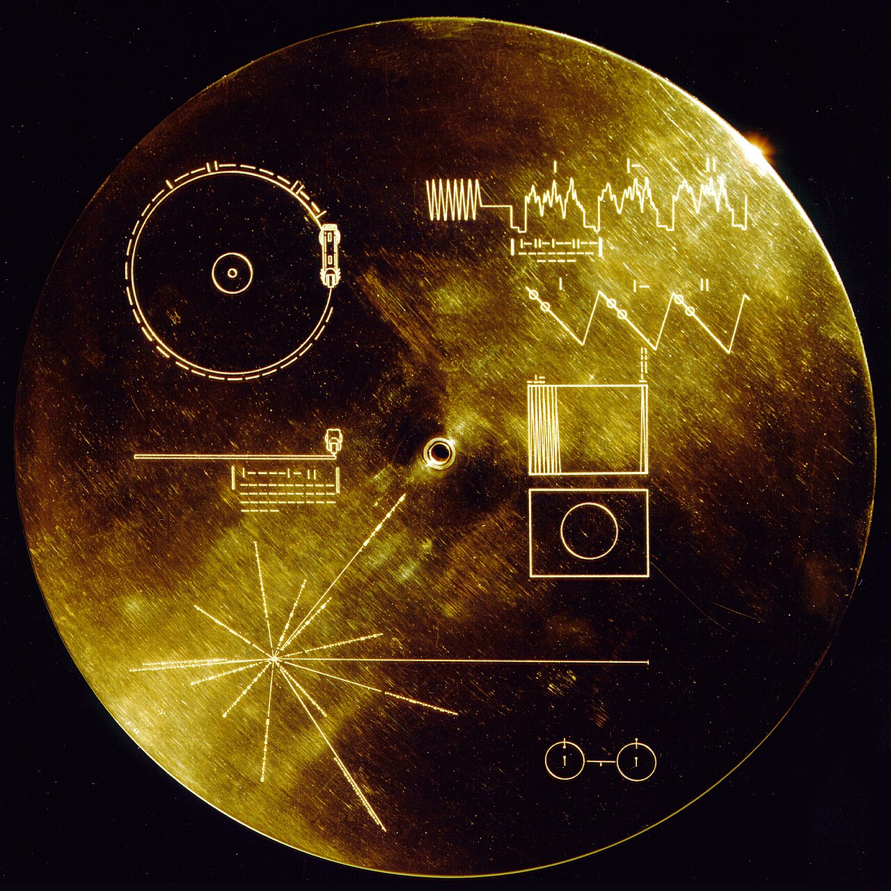 A round gold-colored disc on a black background, etched with simple line diagrams: a record and stylus, wave patterns, a starburst of lines and two small linked circles.
