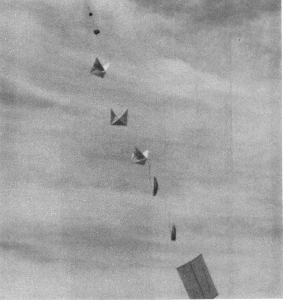 Black-and-white photo of a line of small, box-kite-like radar reflectors made of shiny foil and thin sticks, hanging one below another on a cord against a cloudy gray sky.