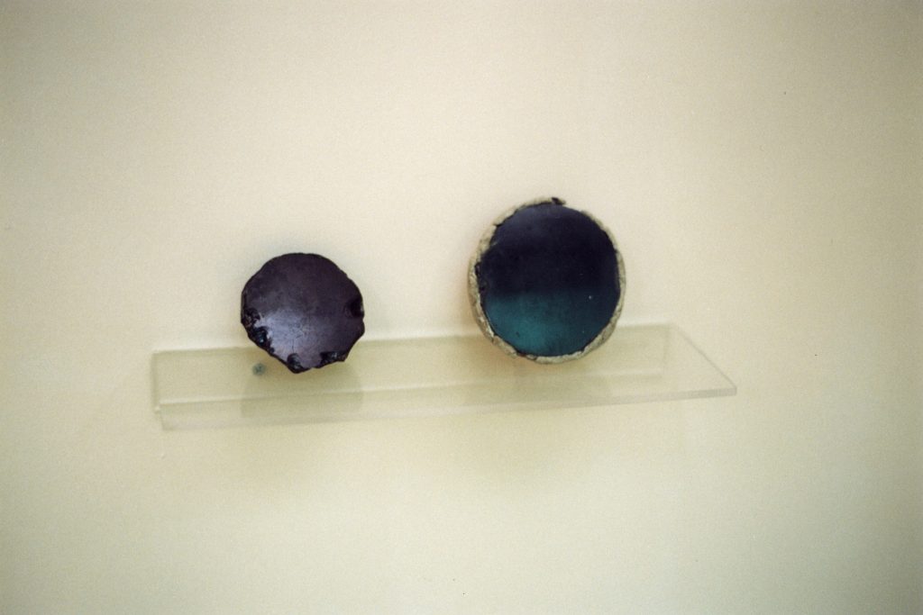 Two small, round mirrors of dark polished obsidian resting on a clear museum shelf.