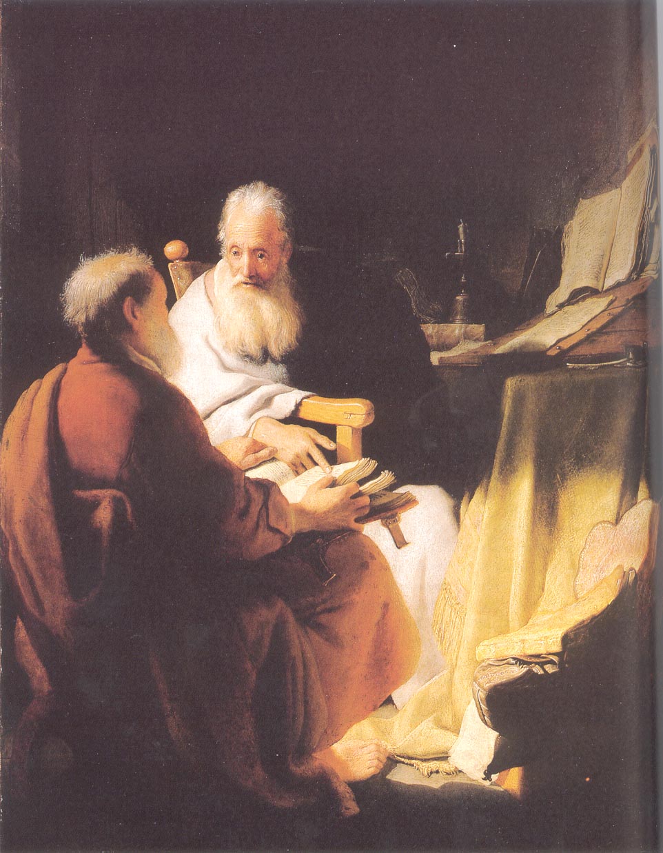 A dim room in which two elderly men sit close together. One, with a long white beard and a white robe, faces the viewer and points at an open book held by the other, who sits with his back half turned to us in a reddish-brown robe. Large open books and a candlestick stand in the light behind them.