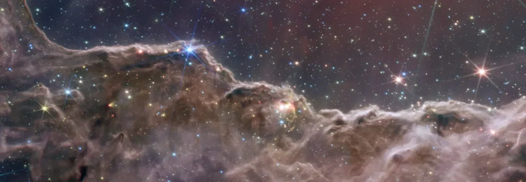Infrared composite of the Cosmic Cliffs, a ridge of gas and dust beneath a field of stars in the Carina Nebula.