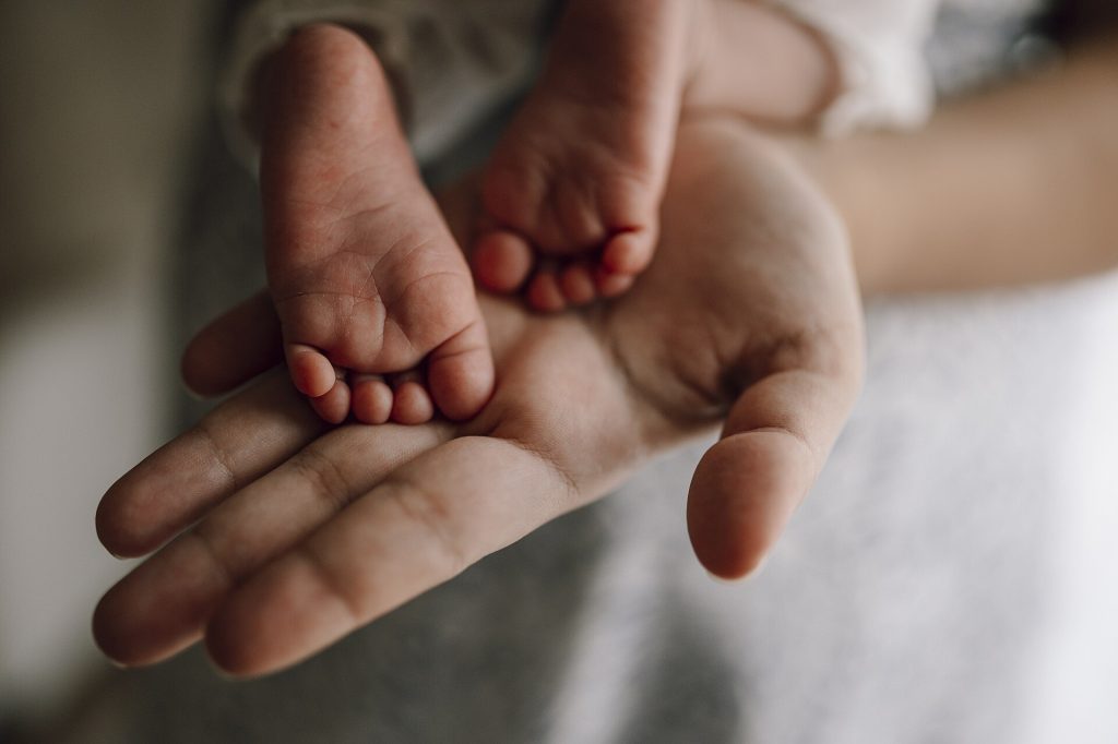 A parent's open hand gently cradling a newborn baby's tiny feet.
