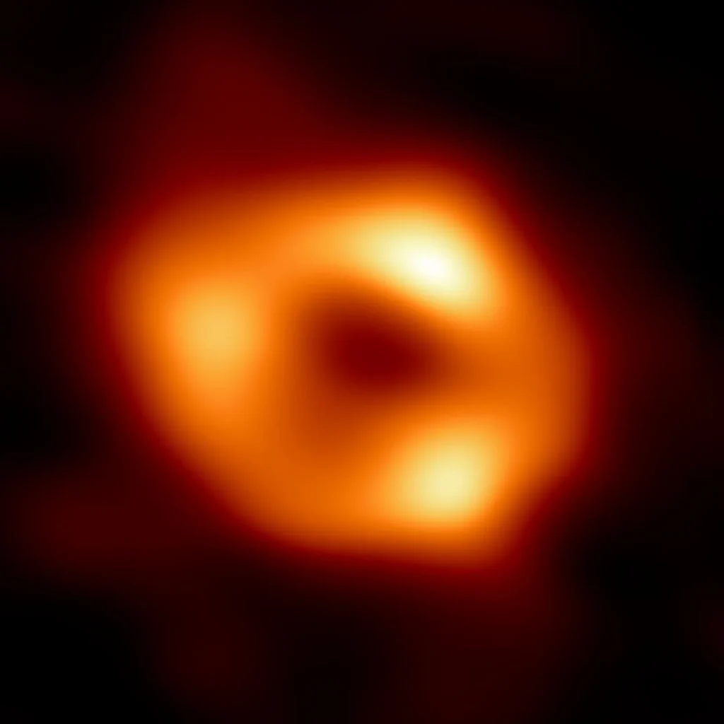 A blurry orange ring of light with three brighter knots, surrounding a dark center, set against a black background.