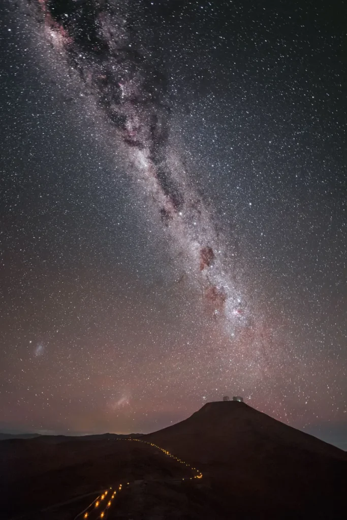 The Milky Way stretches diagonally over a dark desert road leading to ESO’s Paranal Observatory.